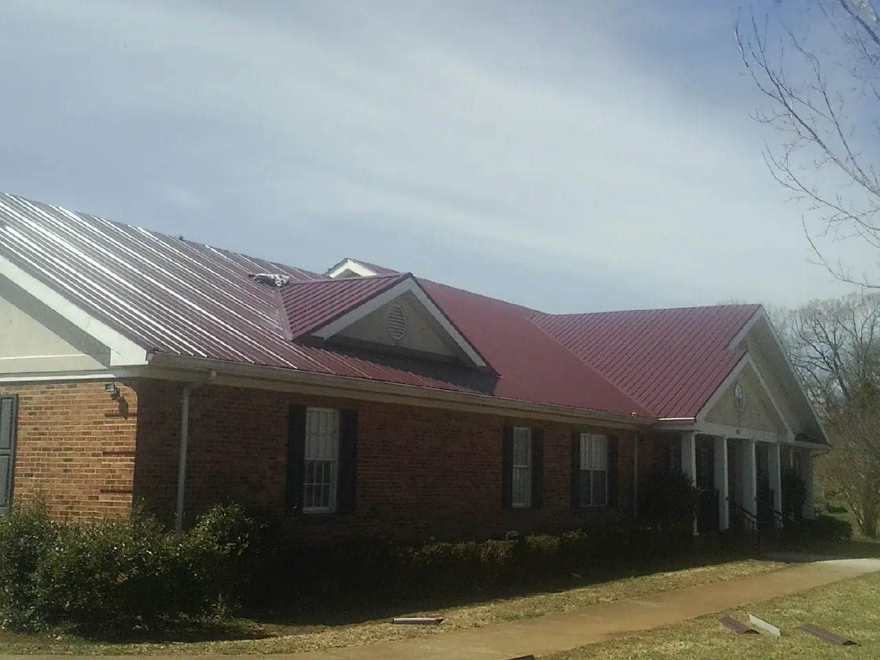 Red metal roof with gabled entries on a long brick building, from a Hail Damage Roof Repair job in South Beach