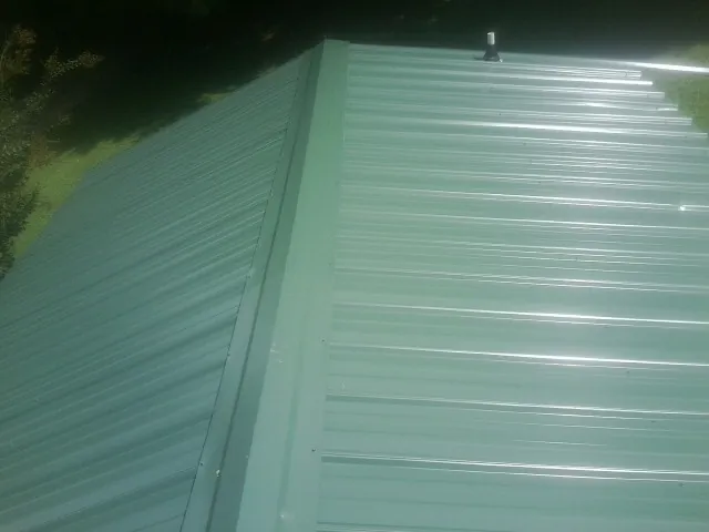 New green metal panels meeting at the ridge of a roof — Flat Roof Repair work by our crew in South Beach