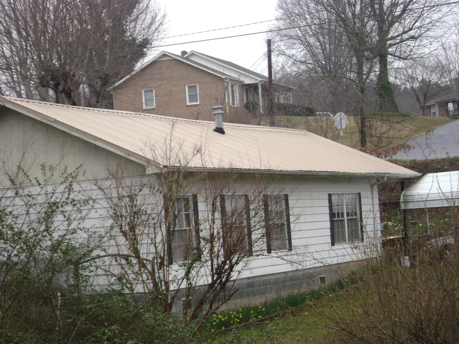 Tan metal roof on a white sided house set into a hillside — Commercial Roofing by Roofing Brothers in South Beach